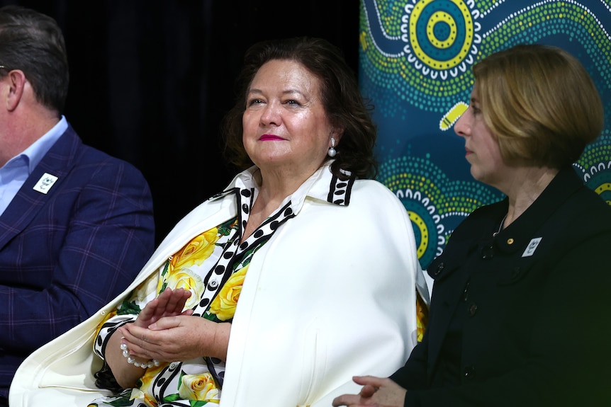 a middle-aged woman wearing a white blazer sitting inside an aquatic centre