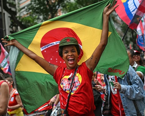 A Lula supporter cheers holding a large Brazilian flag amid a crowd of flags