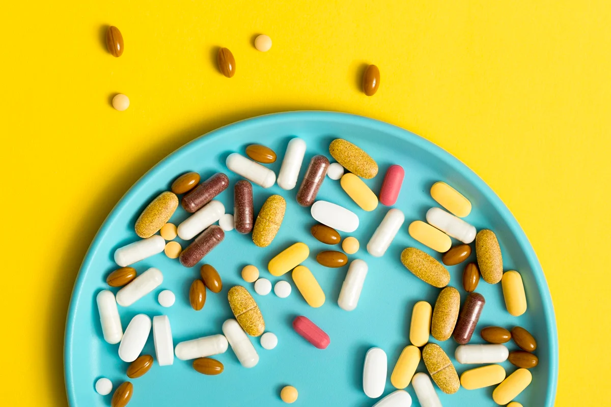 Foto colorida com fundo amarelo, de um prato cor azul, cheio de pílulas que simbolizam suplementos alimentares - Metrópoles