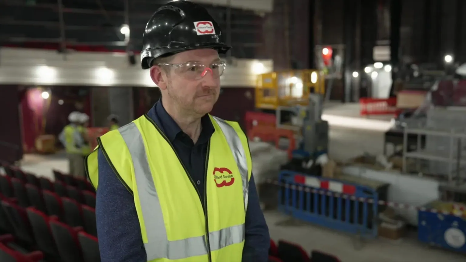 Peter Whittlesea/BBC A man in a yellow hi-vis vest and safety helmet. He is inside a theatre which is undergoing a major refurbishment.